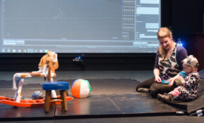 A woman and a small child sit in ECU's Integrated Motion Studio, looking at a collection of toys in front of a large screen.